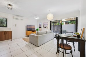 A modern living room with a sofa, dining table, and chairs. There is a TV, a plant, and artwork on the walls. - Beachside Apartment With Secure Parking (Gold Coast)