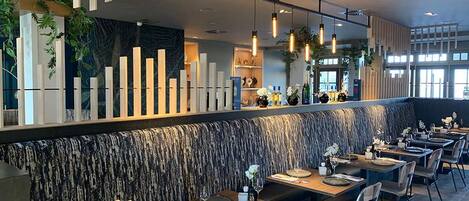 A modern restaurant with a long counter, multiple tables, and a patterned wall.