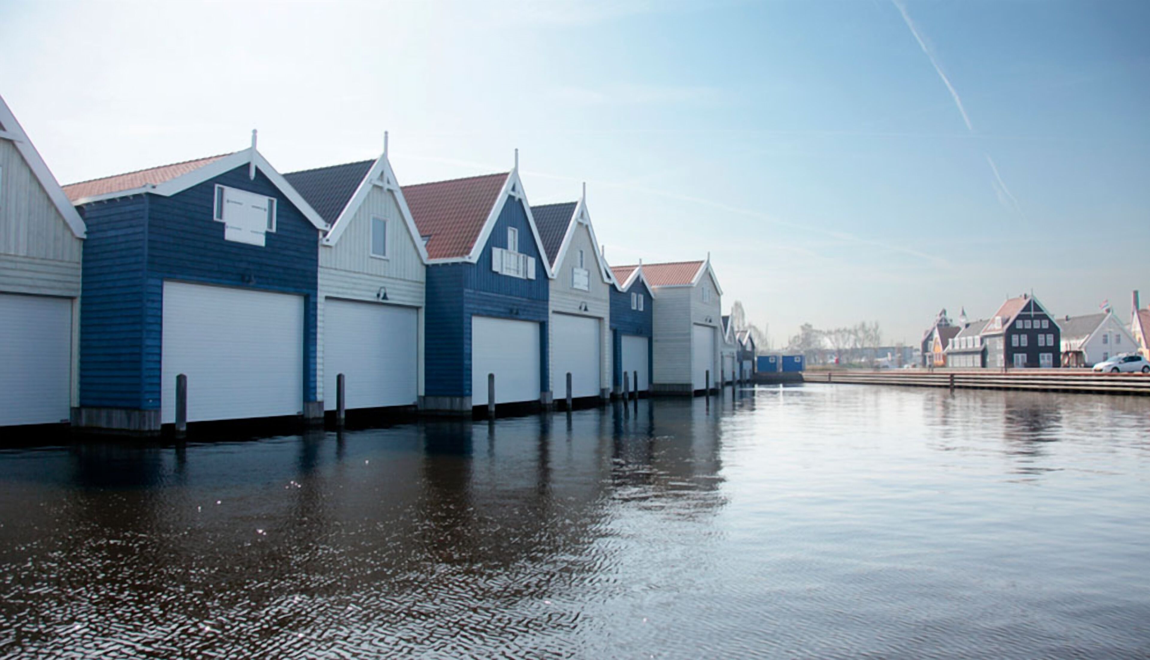 A waterfront property with multiple garage-style buildings, a calm water body, and a clear sky.