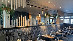 Un restaurante moderno con una barra alargada, varias mesas y una pared con diseño.