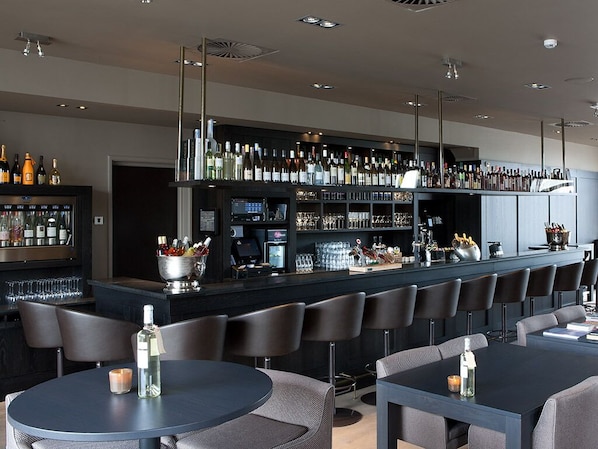 Un bar moderne doté d’un long comptoir, de nombreux espaces pour s’asseoir et d’une variété de bouteilles et de verres exposés.