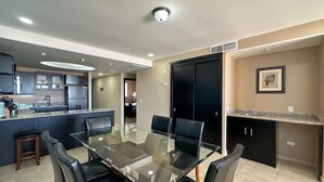 Een moderne keuken met donkere kastjes, een centraal eiland en een eethoek met een glazen tafel en lederen stoelen.