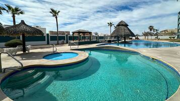 Una piscina cristalina con una zona hundida en el centro, rodeada de sillas de descanso y sombrillas de paja.