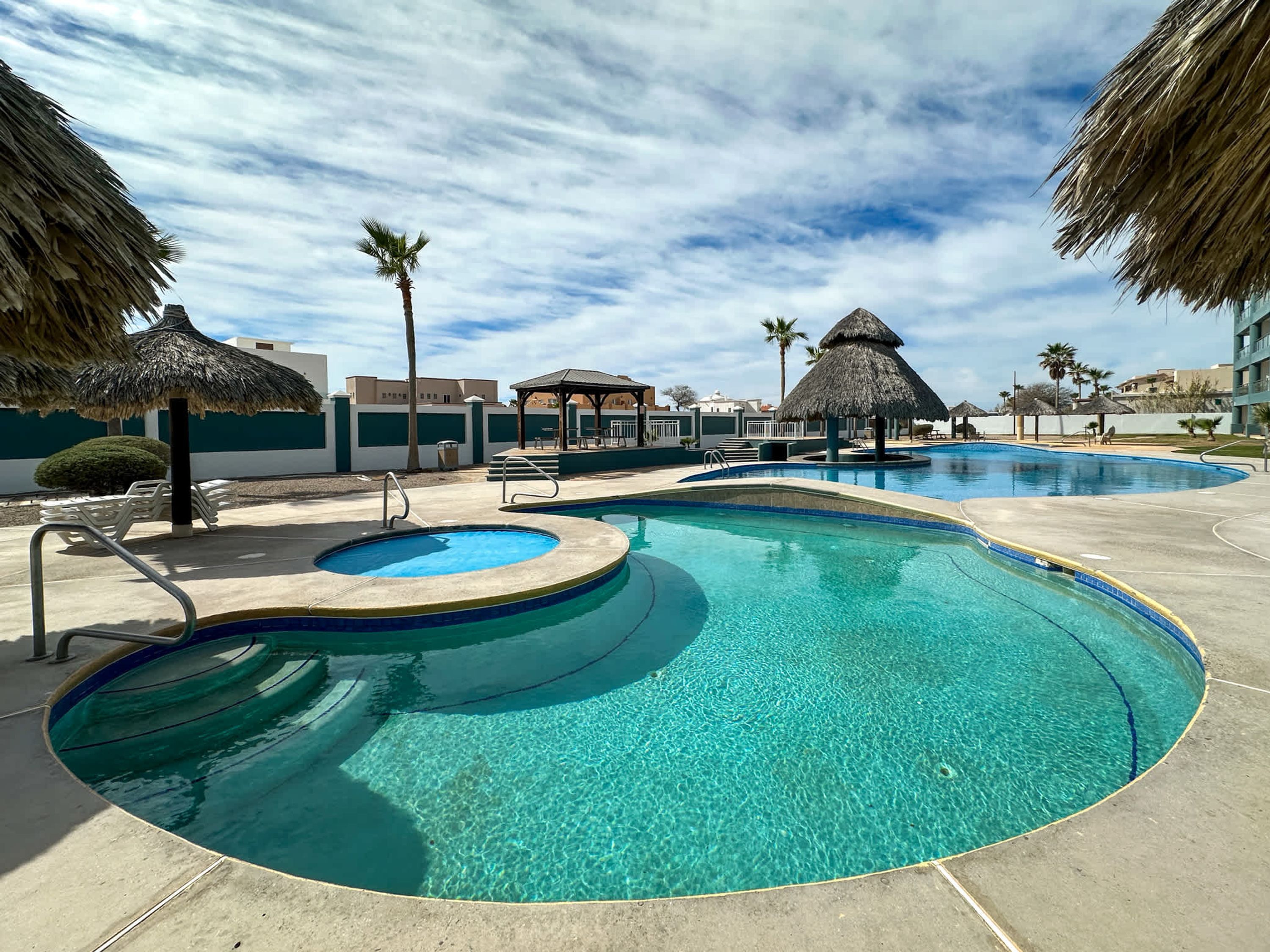Una piscina con diseño circular, rodeada de sillas de descanso y sombrillas de paja.