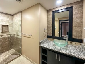 Un baño moderno con cabina de ducha de vidrio, encimera de granito y un espejo grande.