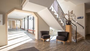 Un intérieur spacieux avec un plafond haut, un escalier et deux fauteuils.