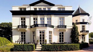 Un grand bâtiment blanc dont la façade porte l’inscription « AVEGOOP », avec de nombreuses fenêtres, un balcon et une petite structure en forme de tour.
