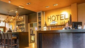 A hotel reception area with a bar, wooden flooring, and a chandelier.