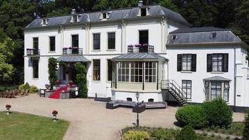 A large, white, two-story building with a symmetrical facade, a central entrance with a red carpet, and a small garden area with a pathway leading to the entrance.
