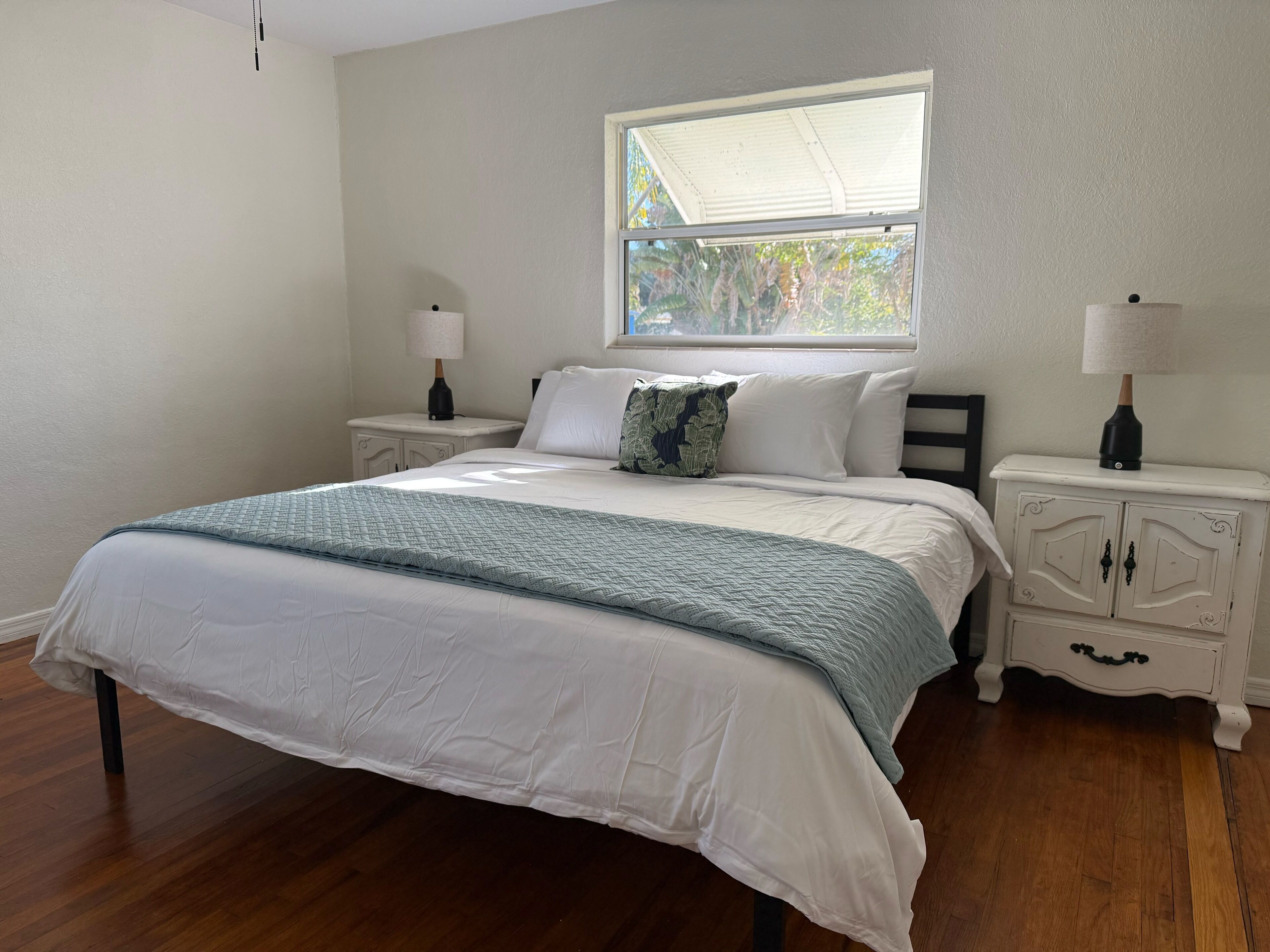 A bedroom with a bed, nightstands, a window, and a dresser.