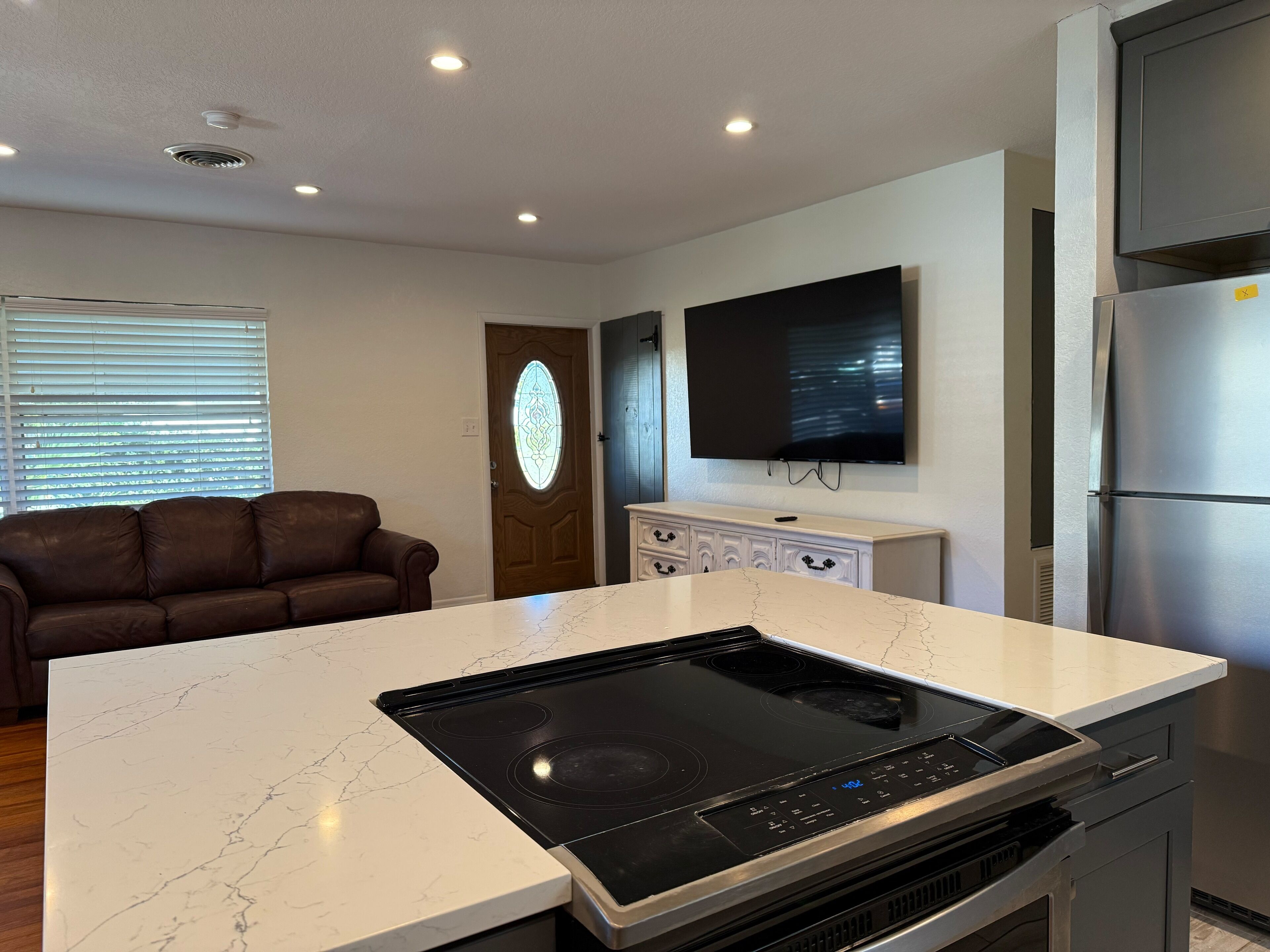 Una cocina moderna con placa vitrocerámica integrada, una isla grande, televisor de pantalla plana y refrigerador de acero inoxidable.