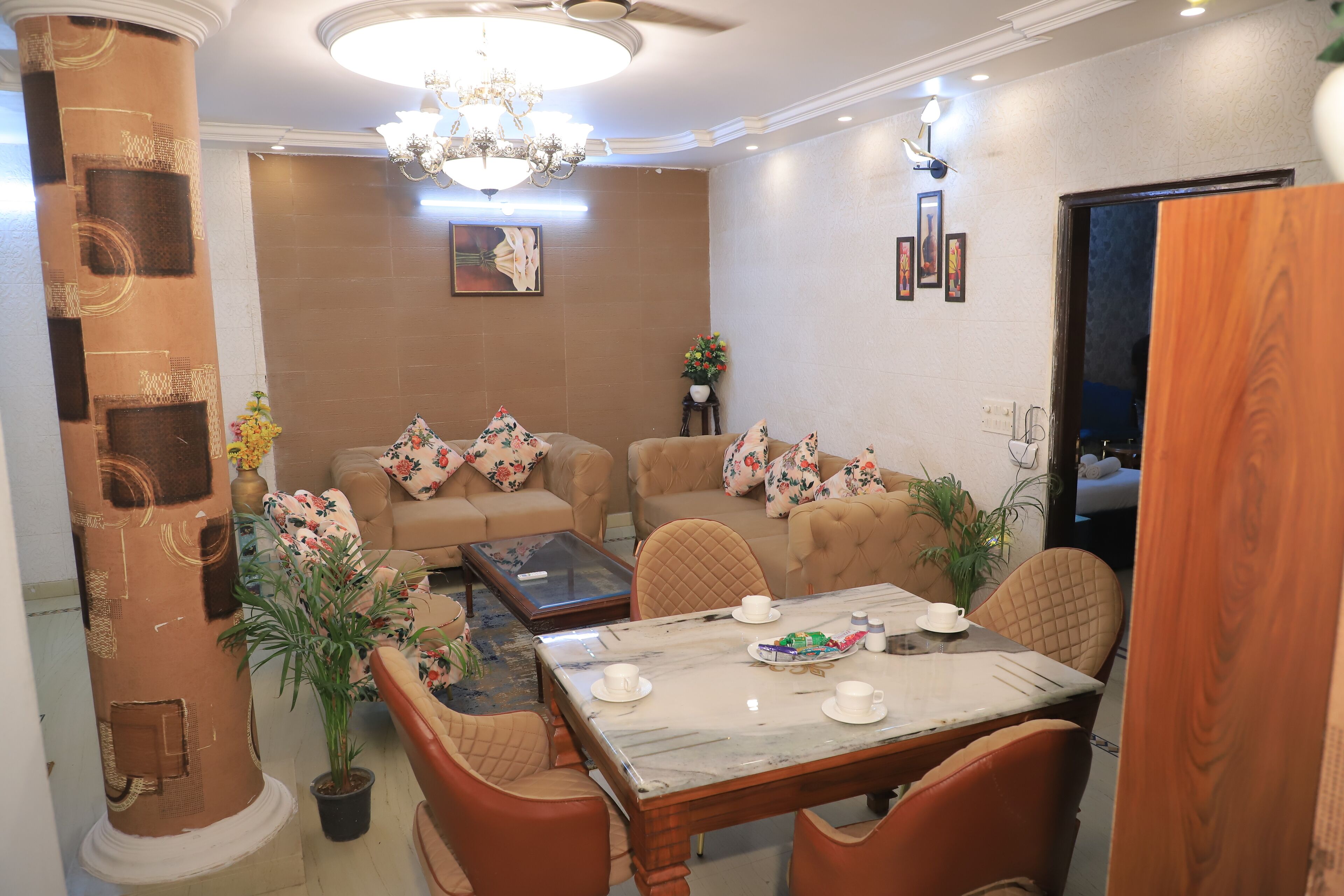 A well-furnished living room with a marble coffee table, floral cushions, and a chandelier.