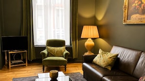A living room with a green armchair, a brown leather sofa, a glass coffee table, a lamp, and a television on a stand. - Cozy Couple Retreat Near Thermes (Spa)