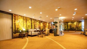 A hotel lobby with a large wall mural of autumn trees, a sofa, chairs, and a reception desk. - Free Parking Included! Garden Relaxation with Trails & Golf Close By (Amersfoort)