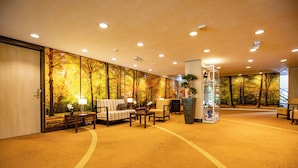 Rebost d'hotel amb un mural gran de paisatge d'arbredes d'autum, un sofà, cadires i una taula d'informació.