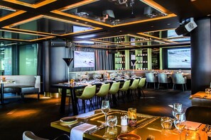 A modern restaurant with a long dining table, multiple screens, and a cozy seating area. - A Relaxing Beachfront Stay with Onsite Dining, Just Steps from Vlissingen’s Best (Vlissingen)