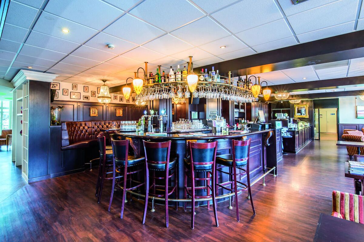 Eine Bar mit hoher Decke, mehreren hängenden Leuchten und einer Bar mit Hockern.