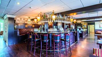 Eine Bar mit hoher Decke, mehreren hängenden Leuchten und einer Bar mit Hockern.