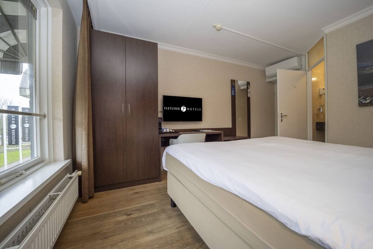 Una habitación de hotel con cama, escritorio, televisor y armario.