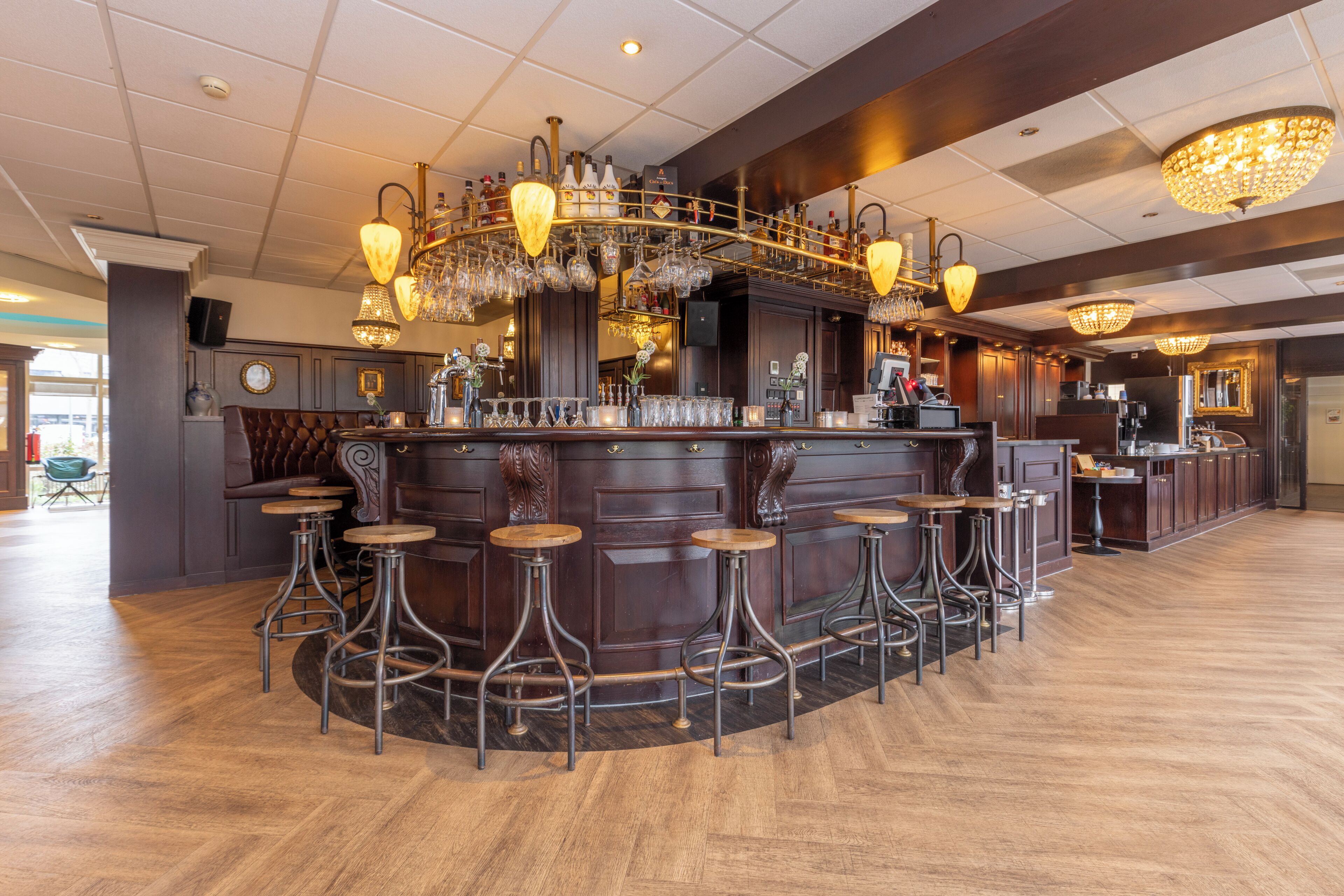A bar area with a wooden bar counter, multiple stools, and hanging light fixtures.