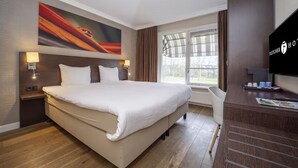 Ein Hotelzimmer mit einem großen Bett, einem Flachbildfernseher, einem Schreibtisch mit Stuhl und einem Vorhangfenster.