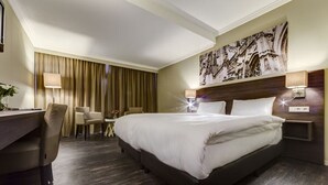 Une chambre d’hôtel avec un grand lit, un bureau, deux chaises, une petite table et un tableau au mur.