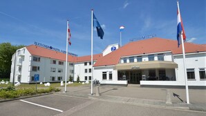 Ein Hotel mit rotem Ziegeldach, Parkplätzen und mehreren Flaggen.