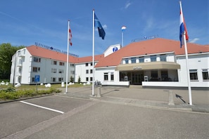 Hotelli, jossa on punatiilinen katto, pysäköintialue ja useita lippuja.