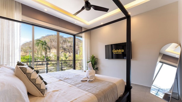 Ein modernes Schlafzimmer mit einem großen Bett, einem Deckenventilator, einem Fernseher und Blick auf eine Berglandschaft.