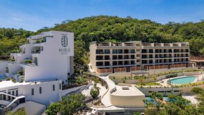 Un hotel moderno con piscina, rodeado de exuberante vegetación y una colina boscosa.