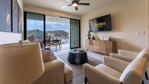 Una sala de estar moderna con un sofá, sillones, una mesa de centro, un televisor montado en la pared y un balcón con vistas a las montañas.
