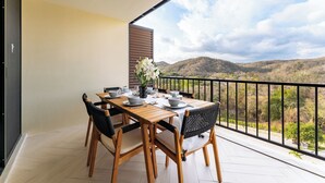 Un balcón con una mesa de madera dispuesta para comer, un florero con flores blancas y vistas a un paisaje montañoso.