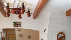 A dining area with a round table, a vase of flowers, a fireplace, and a kitchen in the background. - Provencal House (Bormes les mimosas)