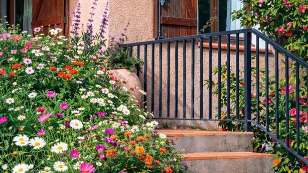 A building with a textured facade, wooden double doors, and a black metal staircase leading to a balcony. - Provencal House (Bormes les mimosas)