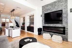 A modern living room with a fireplace, a TV mounted on the wall, and a dining area with a kitchen in the background. - Centrally Located in Denver- 4Bed 4Bath (Denver)