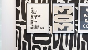 A wall with abstract black and white patterns, a framed sign with multilingual greetings, and a decorative plant in a textured vase. - Global Retreat in the Rockies | Central Location (Denver)