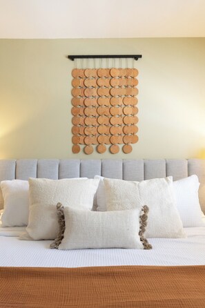 Ein Bett mit grauem Kopfteil, weißen Kissen und einer an der Wand befestigten, runden Holzdeko.