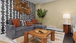 A modern living room with a grey sofa, patterned cushions, a wooden coffee table, a large plant, and a lamp on a side table. - Global Retreat in the Rockies | Central Location (Denver)