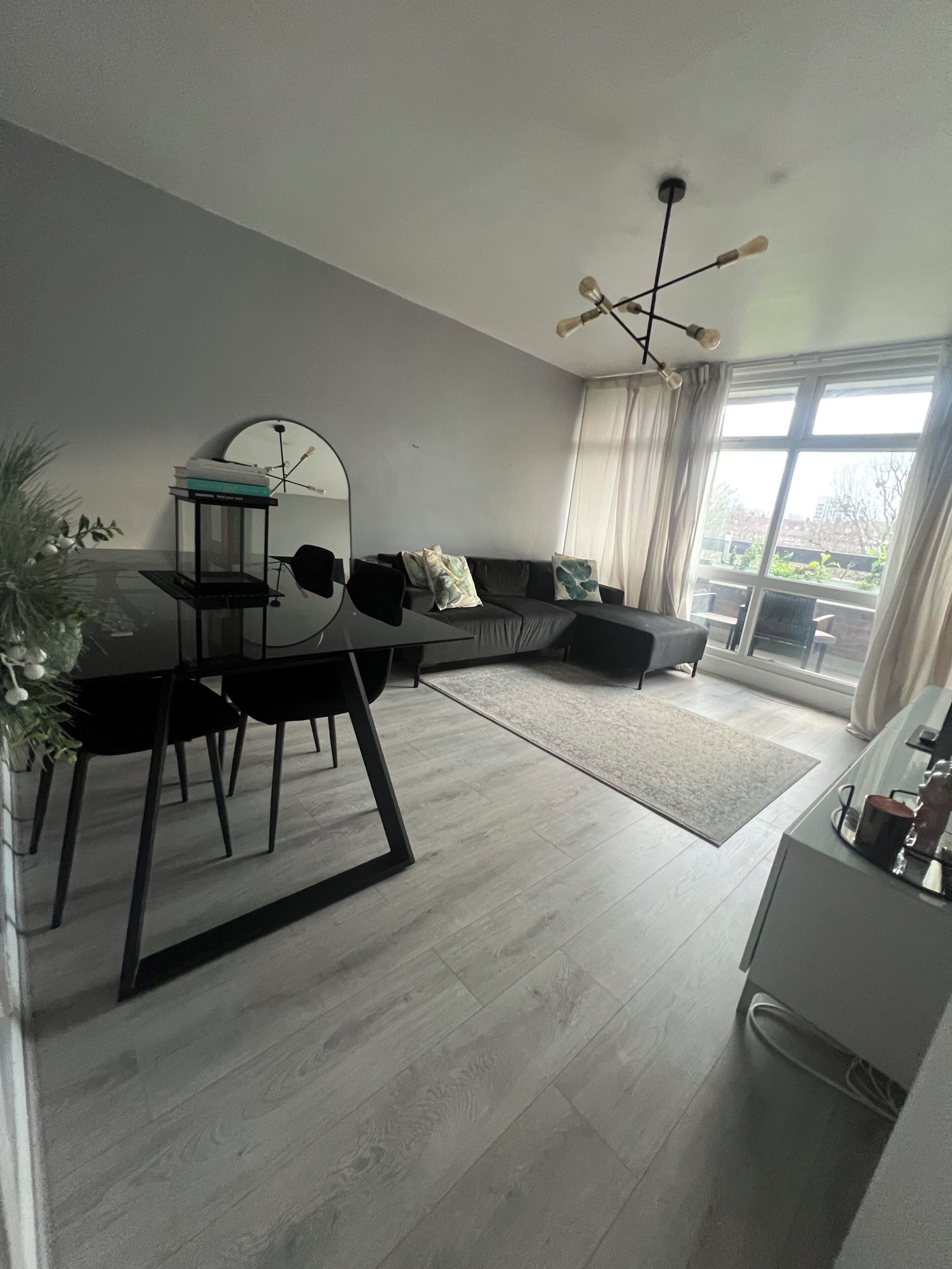 Una sala de estar moderna con una mesa de comedor, sillas negras, un sofá negro y un ventanal con cortinas.