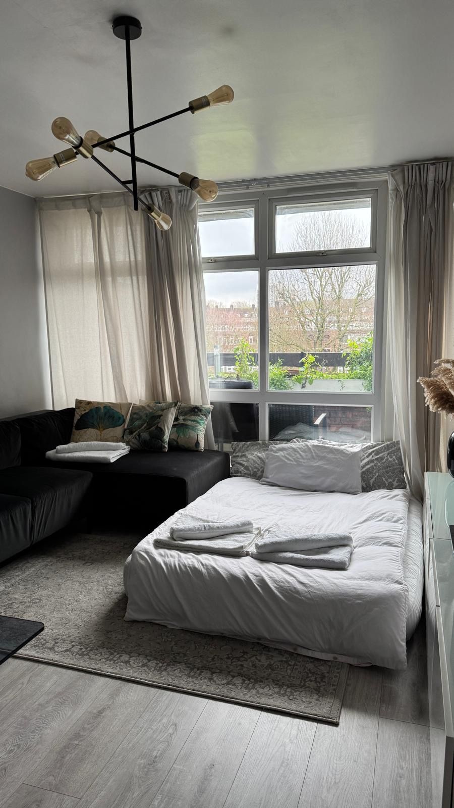 A modern bedroom with a bed, a sofa, a large window, and a ceiling light fixture.
