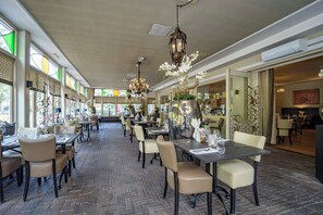 Ein Restaurant mit Backsteinböden, beigen Stühlen und Tischen, die mit Weingläsern und Tellern gedeckt sind.