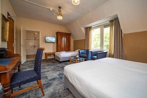 A hotel room with a large bed, a desk with a chair, a television, and a window with curtains.