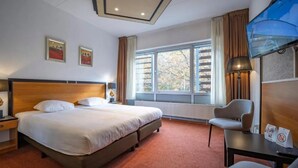 Une chambre d’hôtel avec un grand lit, une chaise, un bureau et une fenêtre avec des rideaux.