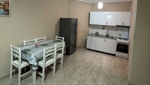 A compact kitchen with white cabinets, a black refrigerator, a gas stove, and a dining table with chairs.