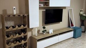 A living room with a TV mounted on a white cabinet, a wine rack, a small plant, and a mirror.