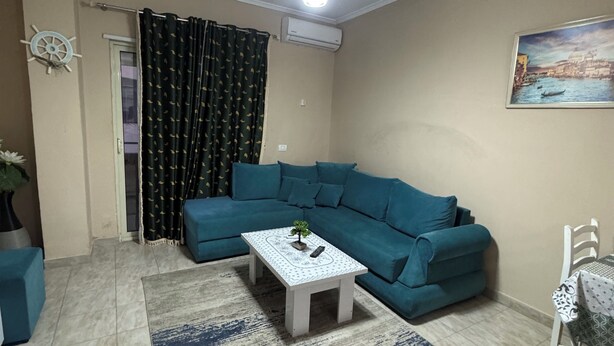 A living room with a teal sofa, a white coffee table with a small plant, a patterned rug, and a ceiling light fixture.