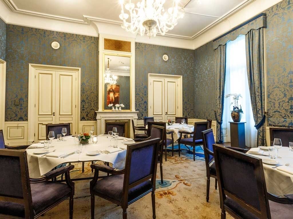 Una sala da pranzo formale con diversi tavoli e sedie, un lampadario e un camino.
