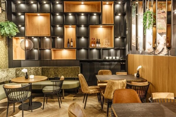 Un restaurante con estanterías de madera y color negro que exhiben botellas y vasos, rodeado de asientos acolchados y una zona de bar.