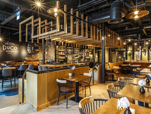 A modern bar and dining area with wooden furniture, bar stools, and hanging lights.