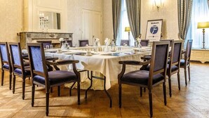 Un comedor formal con una gran mesa redonda, múltiples sillas, una araña y una chimenea.